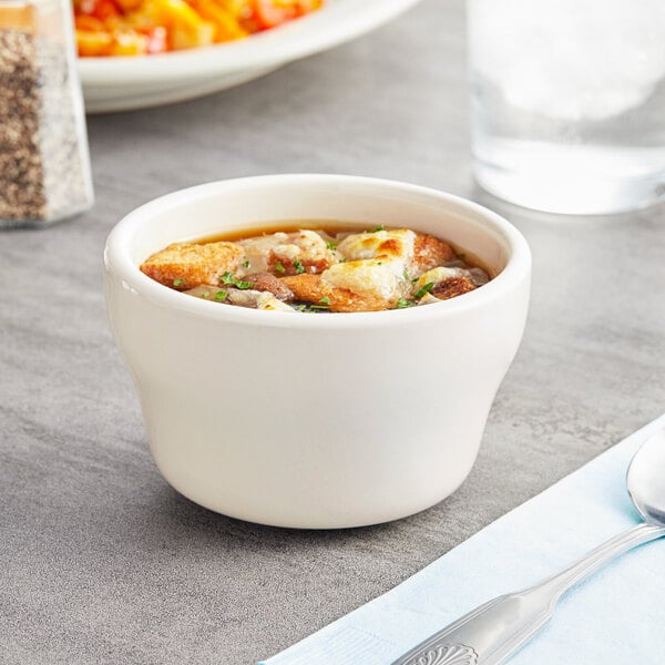 An Acopa ivory stoneware bouillon cup with a spoon on a table.