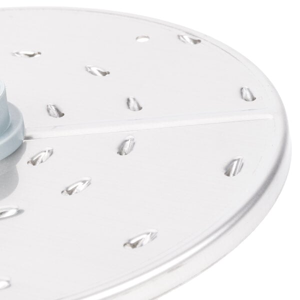 A close-up of a Robot Coupe 1/8" grating/shredding disc, a circular metal object with holes in it.