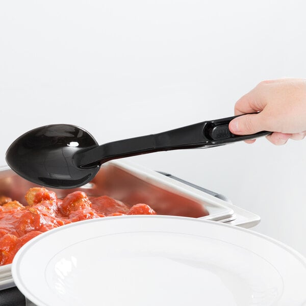 A person using a Cambro black high heat solid salad bar spoon to serve food.