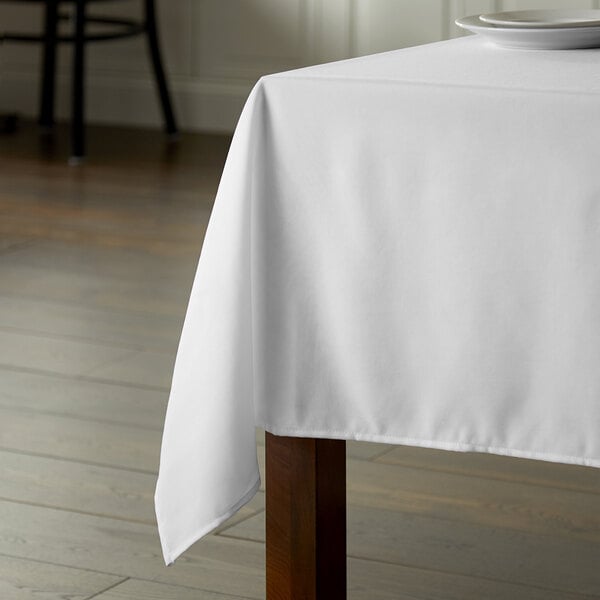 A wooden table with a white Intedge rectangular tablecloth.