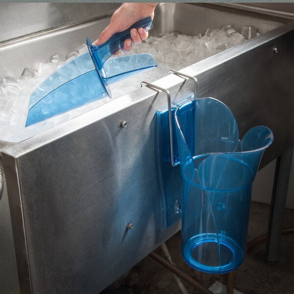 A hand pours ice from a blue San Jamar Saf-T-Ice scoop holder into a blue container.