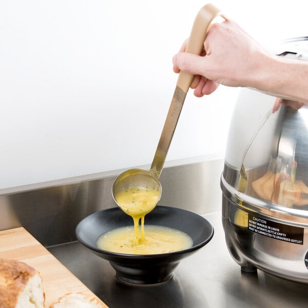 A hand using a Vollrath Jacob's Pride ladle to pour soup into a bowl.