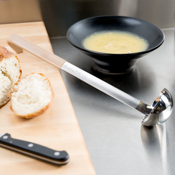A bowl of soup and a ladle on a cutting board.
