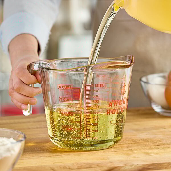 A person pouring liquid into an Anchor Hocking clear glass measuring cup.