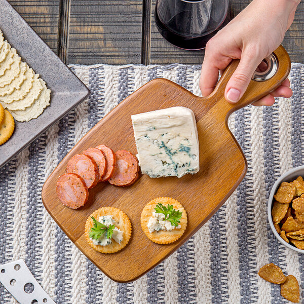 A hand holding a Tablecraft acacia wood bread board with crackers and cheese.