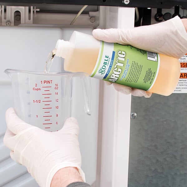 A person in gloves pouring Noble Chemical Arctic Ice Machine Cleaner from a container into a measuring cup.