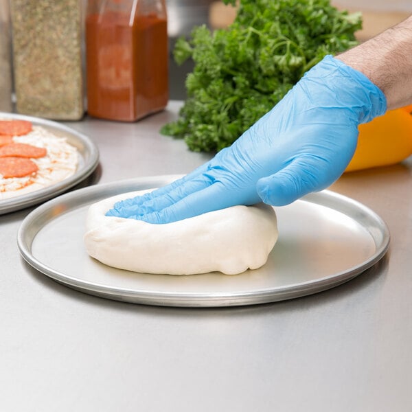 chef pressing pizza dough on to tin pizza pan