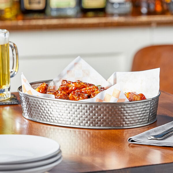 A Tablecraft oval stainless steel platter with a plate of chicken wings on a table.