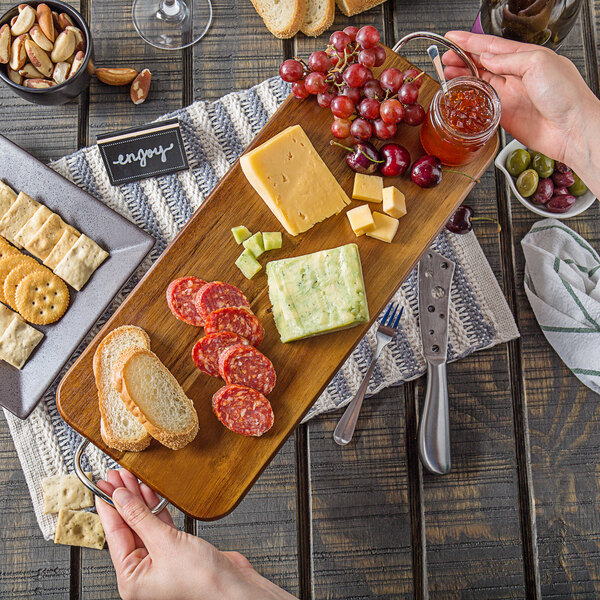 A person holding a wooden Tablecraft rectangular display board with food on it.