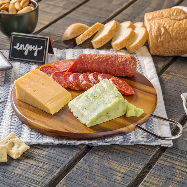 A Tablecraft acacia wood display board with cheese, bread, and crackers on a table.