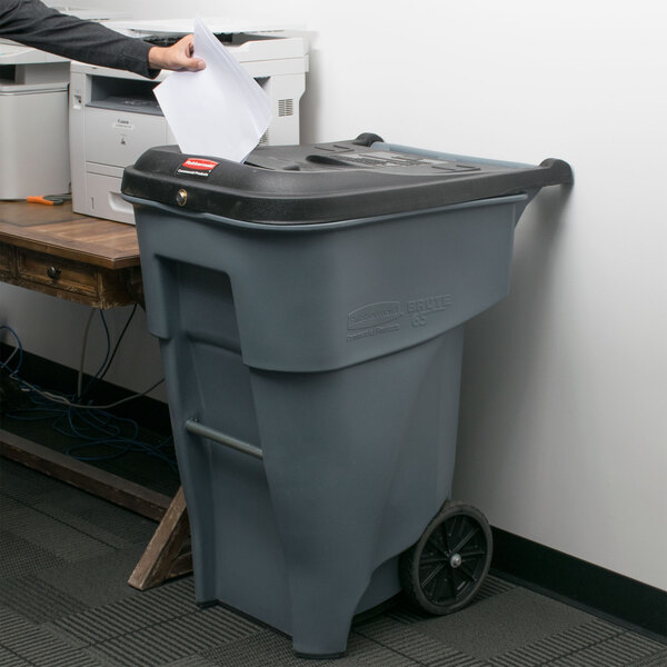 A person putting a confidential document into a Rubbermaid Brute trash can with a locking lid.