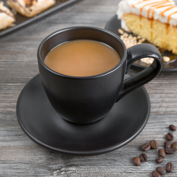 A black Libbey porcelain mug filled with coffee on a plate with cake.