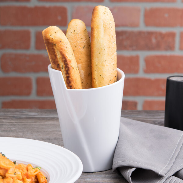 A white Elite Global Solutions small spiral crock filled with bread on a table next to a plate of food.