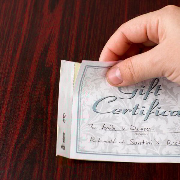 A hand holding an Adams GFTC1 carbonless gift certificate.