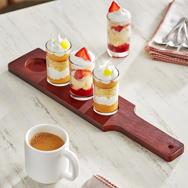 An Acopa mahogany tasting flight paddle with Straight Up Tasting Glasses on a table with desserts and a white mug of brown liquid.