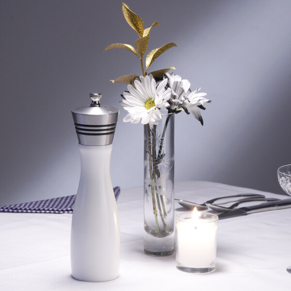 A white Chef Specialties pepper mill on a table with flowers and a candle.