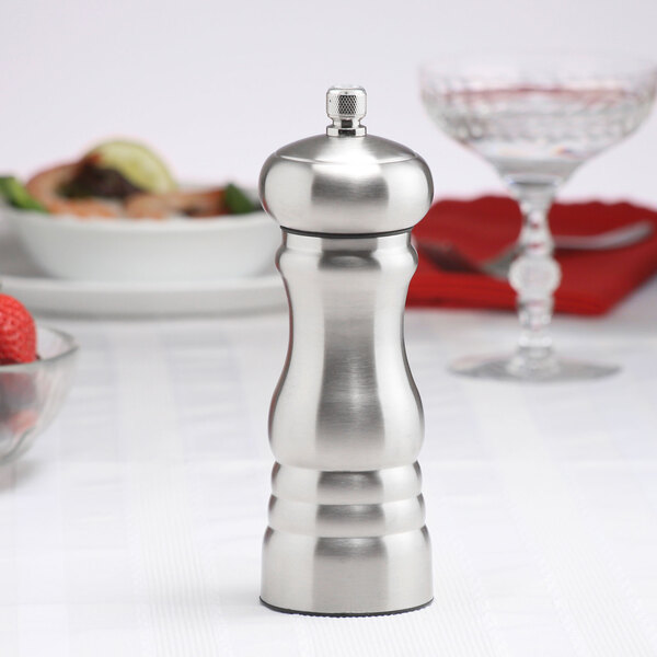 A Chef Specialties stainless steel salt mill on a table with a glass of wine.