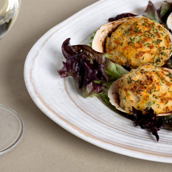 An off white Elite Global Solutions Della Terra irregular oval serving dish with a plate of food on a table.