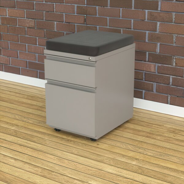 A grey file cabinet with a cushion on top.