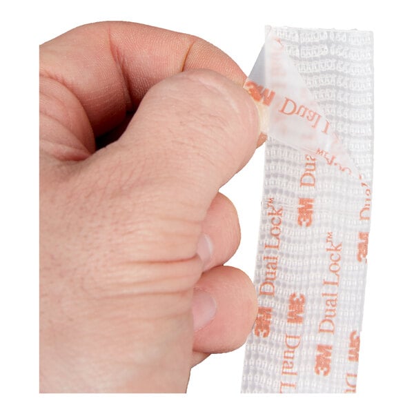 A hand peeling the backing off a strip of 3M Scotch 1-inch by 48-inch clear extreme fastener.