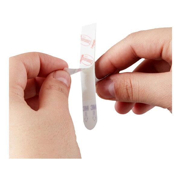 A person peeling the backing off a Command adhesive strip.