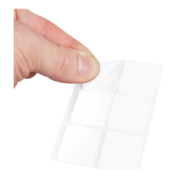 A hand holding a sheet of small white adhesive fastener squares.