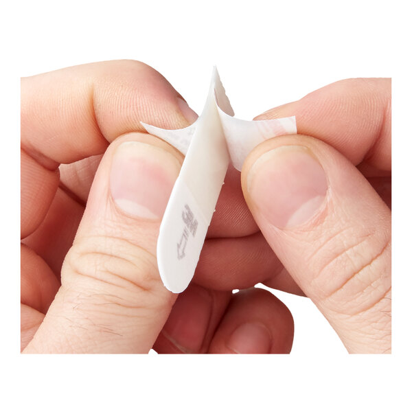 A person peeling the adhesive backing off a small white Command™ strip.