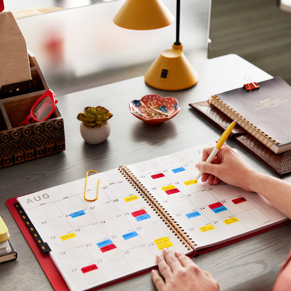 A hand using a pen to write on Post-It tabs in a calendar.
