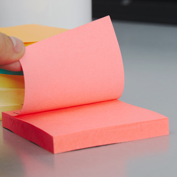 A hand holding a stack of yellow and pink Post-It notes.