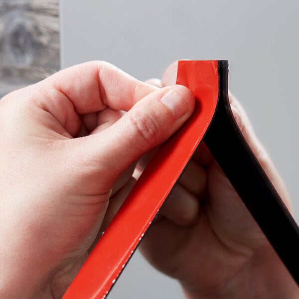 A person using 3M Scotch black mounting tape to hang a red and black frame.