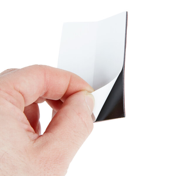 A hand using a 3M Scotch mounting strip to hang a piece of paper.