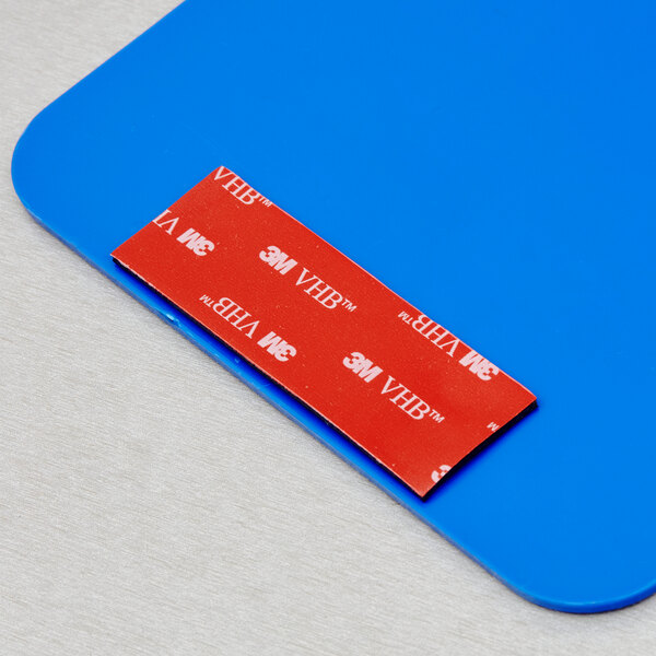 A red rectangular 3M Scotch mounting strip on a blue surface.
