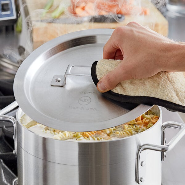 A hand holding a white and black cloth cleaning a Choice aluminum pot lid.