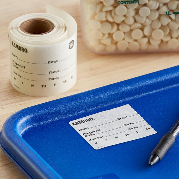 A blue tray with a roll of white Cambro dissolvable product labels with black text on it.