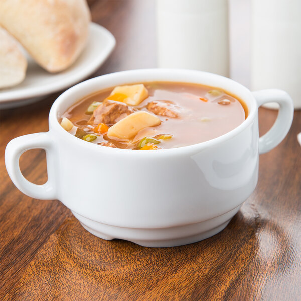 An Arcoroc white porcelain soup bowl filled with soup on a table.