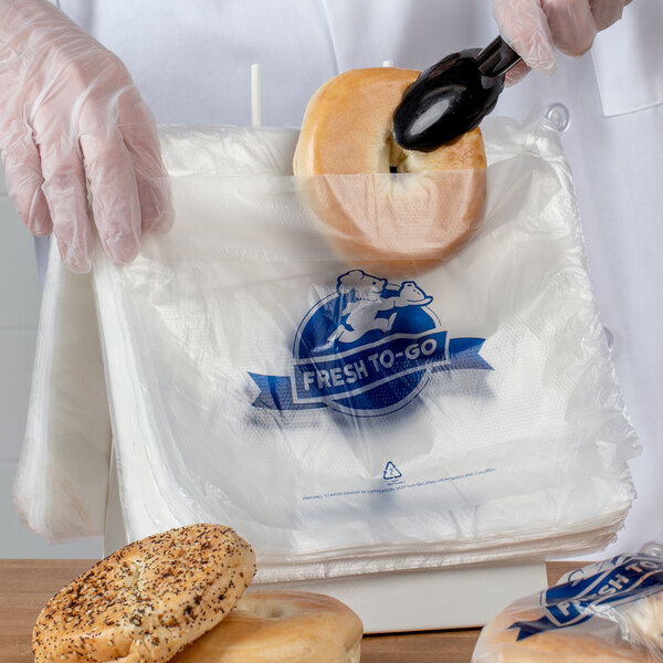 Bagel being placed into a plastic flip top deli bag
