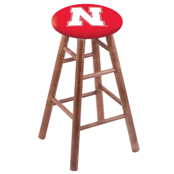 A wooden Holland Bar Stool with a red seat and the University of Nebraska logo on the seat.