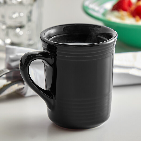 A close-up of a Tuxton Concentrix black mug with a handle on a table with a green bowl of food.