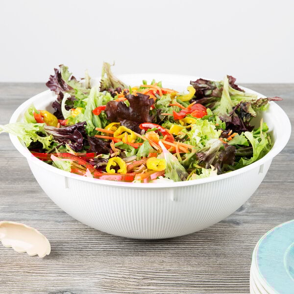A white high profile plastic catering bowl filled with salad on a table.