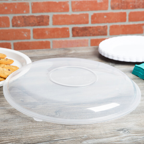 A clear plastic Fineline catering bowl lid on a table over a plate of cookies.