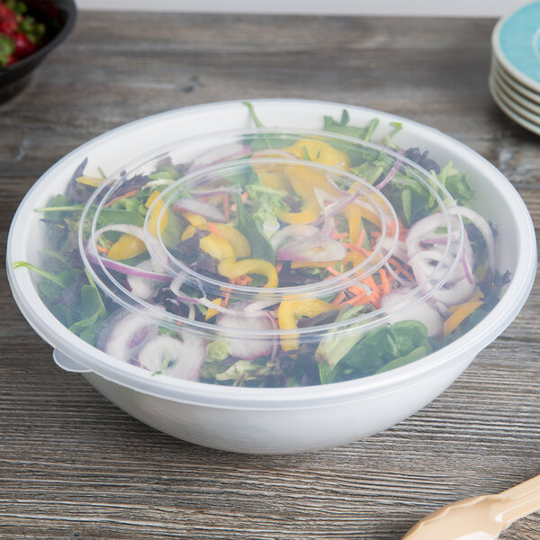 A Fineline clear plastic catering bowl with a lid on a table with salad inside.
