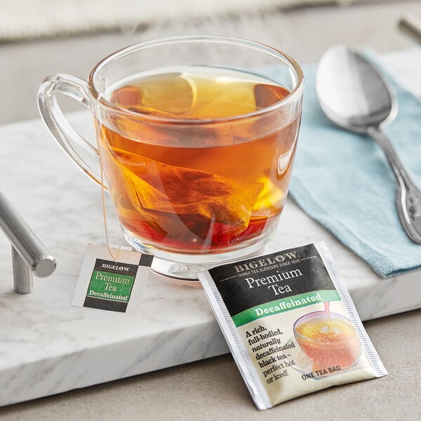 A glass cup of Bigelow decaffeinated tea with a tea bag on a saucer.