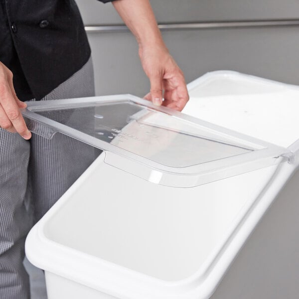 A hand holding a clear plastic lid over a white container.