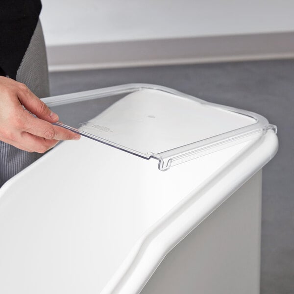 A hand holding a plastic lid over a Cambro ingredient bin.