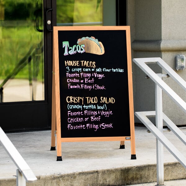 An Aarco oak A-Frame sign with black write-on board on a sidewalk.