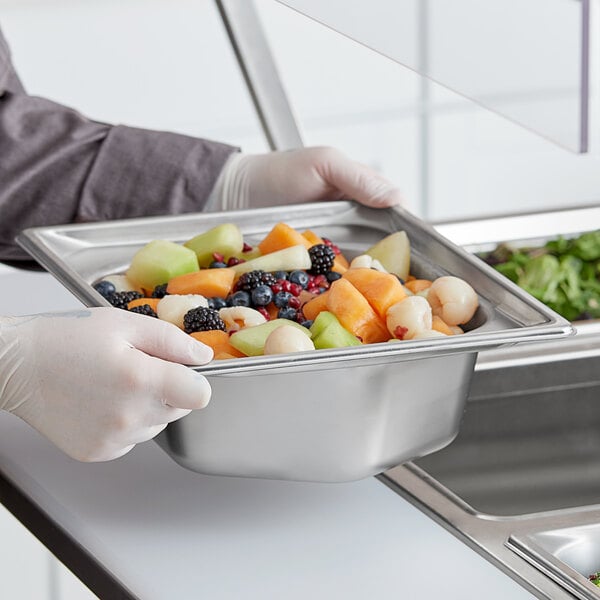 A person in gloves holding a Vollrath stainless steel hexagon pan filled with fruit.