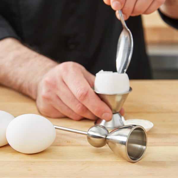 A hand using a Matfer Bourgeat stainless steel egg topper to scoop an egg.