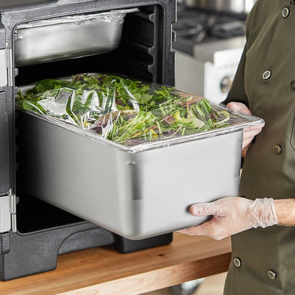 A person in a chef's uniform holding a Hobart stainless steel catch pan of food.