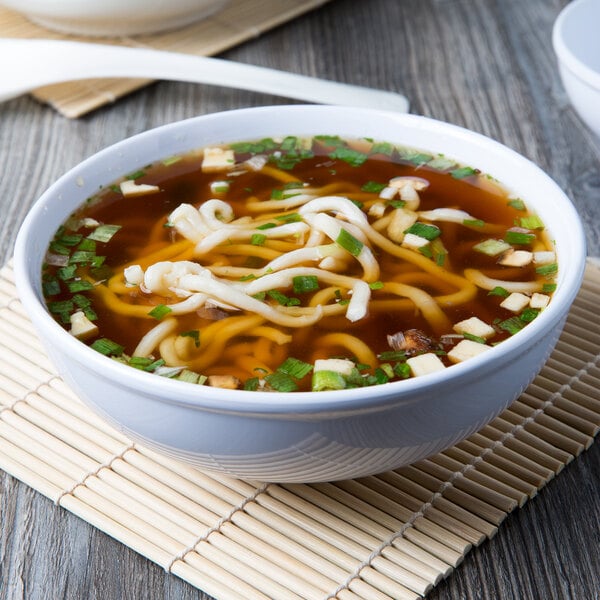 A bowl of soup with noodles and green onions served in a white Thunder Group Pho Noodle Bowl.