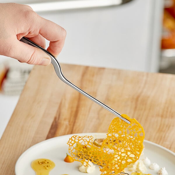 A person using Mercer Culinary offset plating tongs to place food on a plate.